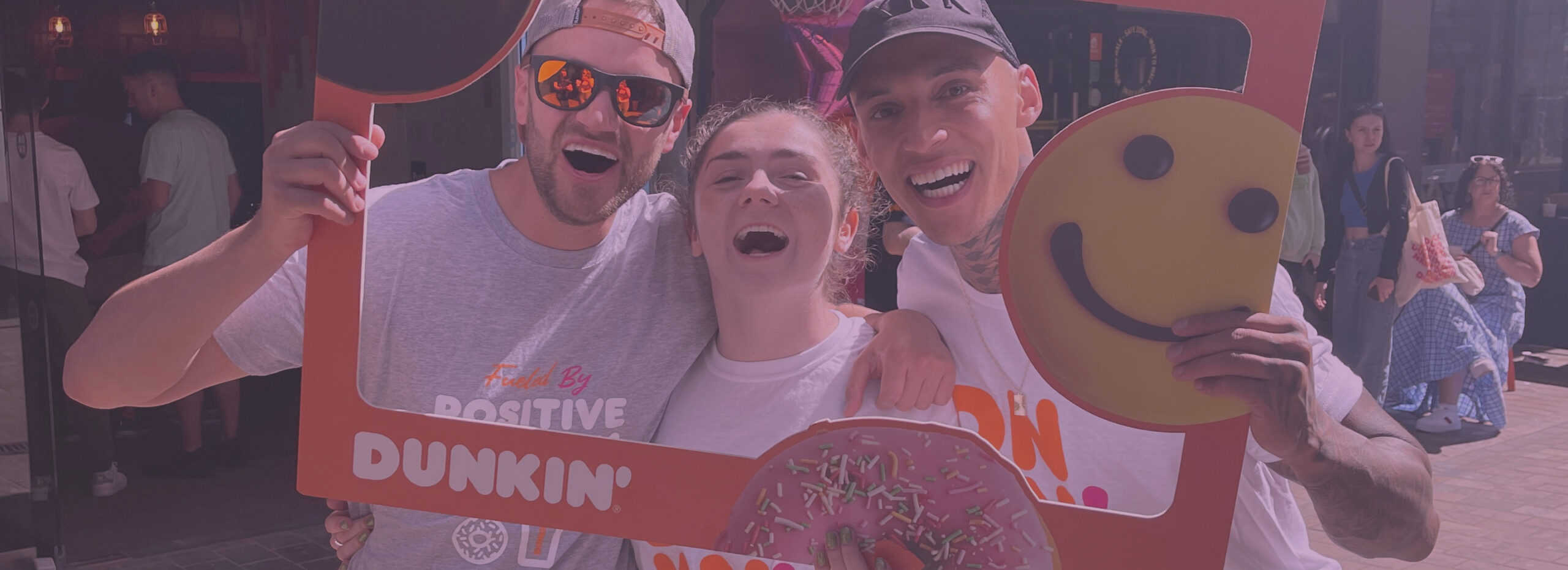 Three people holding a Dunkin' donuts frame