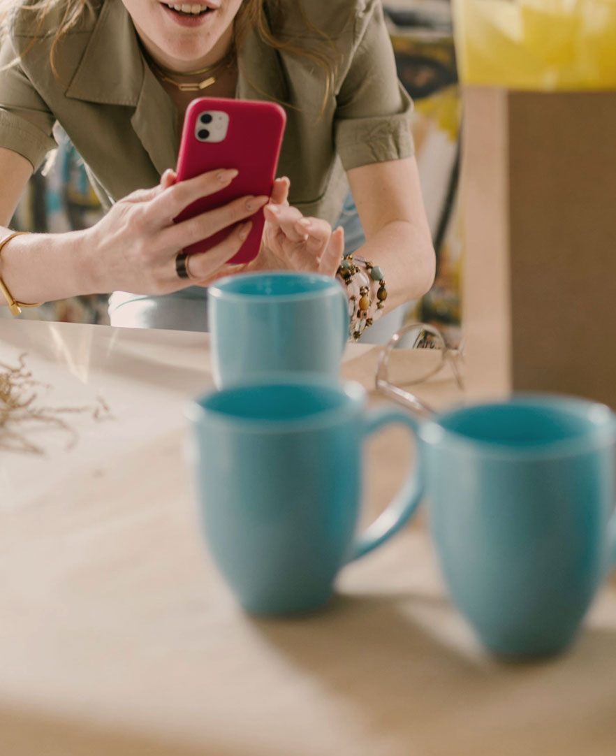 A woman take a picture of the mugs in front of her with her smart phone
