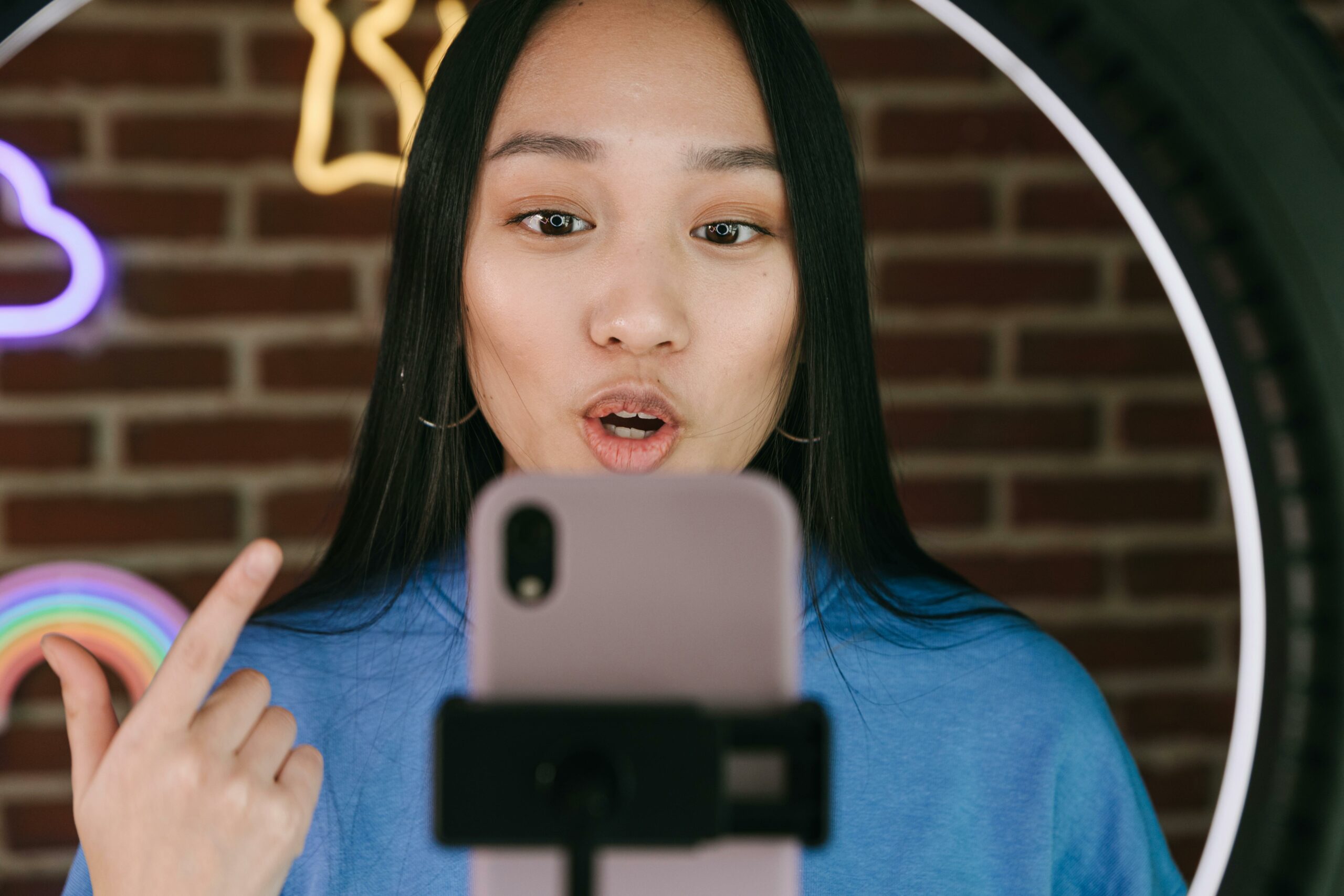 An influencer woman stands in front of a ring light with a phone in front of her recording