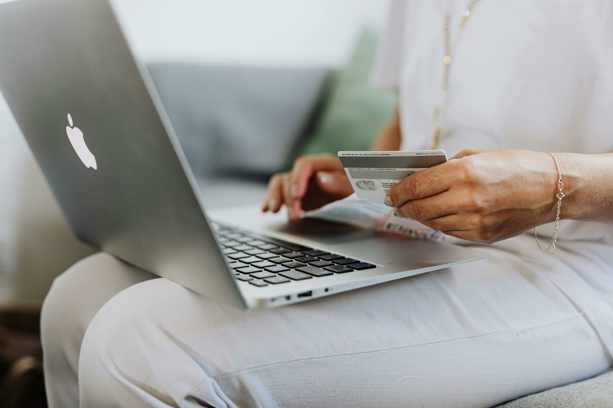 A woman sits with her laptop on her lap holding a credit card, online shopping